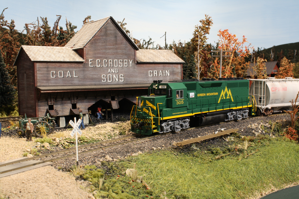 A model of a green diesel locomotive passes by a coal dealer