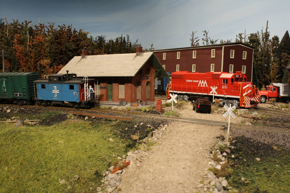 A model of a red diesel locomotive passes behind a station