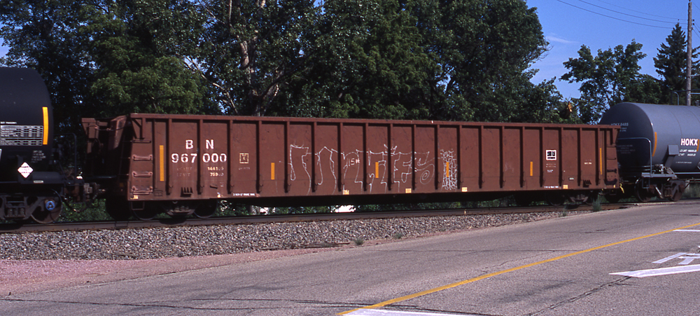 Color photo of Oxide Red gondola in a train by grade crossing.