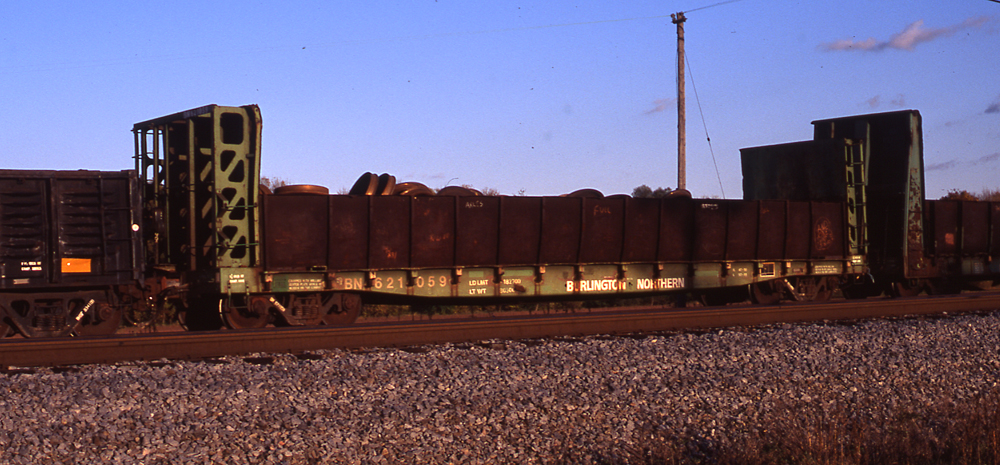 Color photo of green bulkhead flatcar with rusty metal sides.