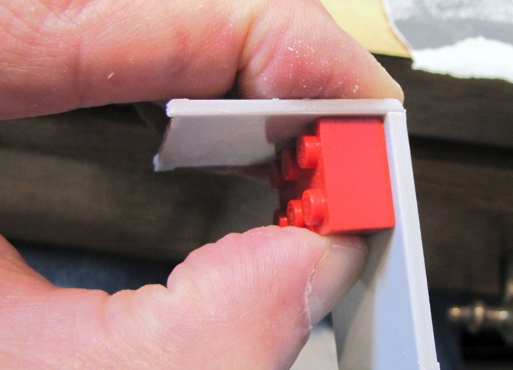 Man holding parts of car kit with Lego brick in corner joint.