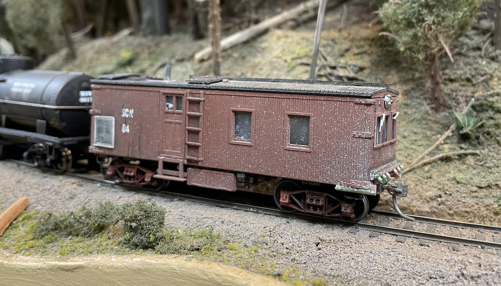 Small model of a brown railroad car with large windows on mountain side railroad track