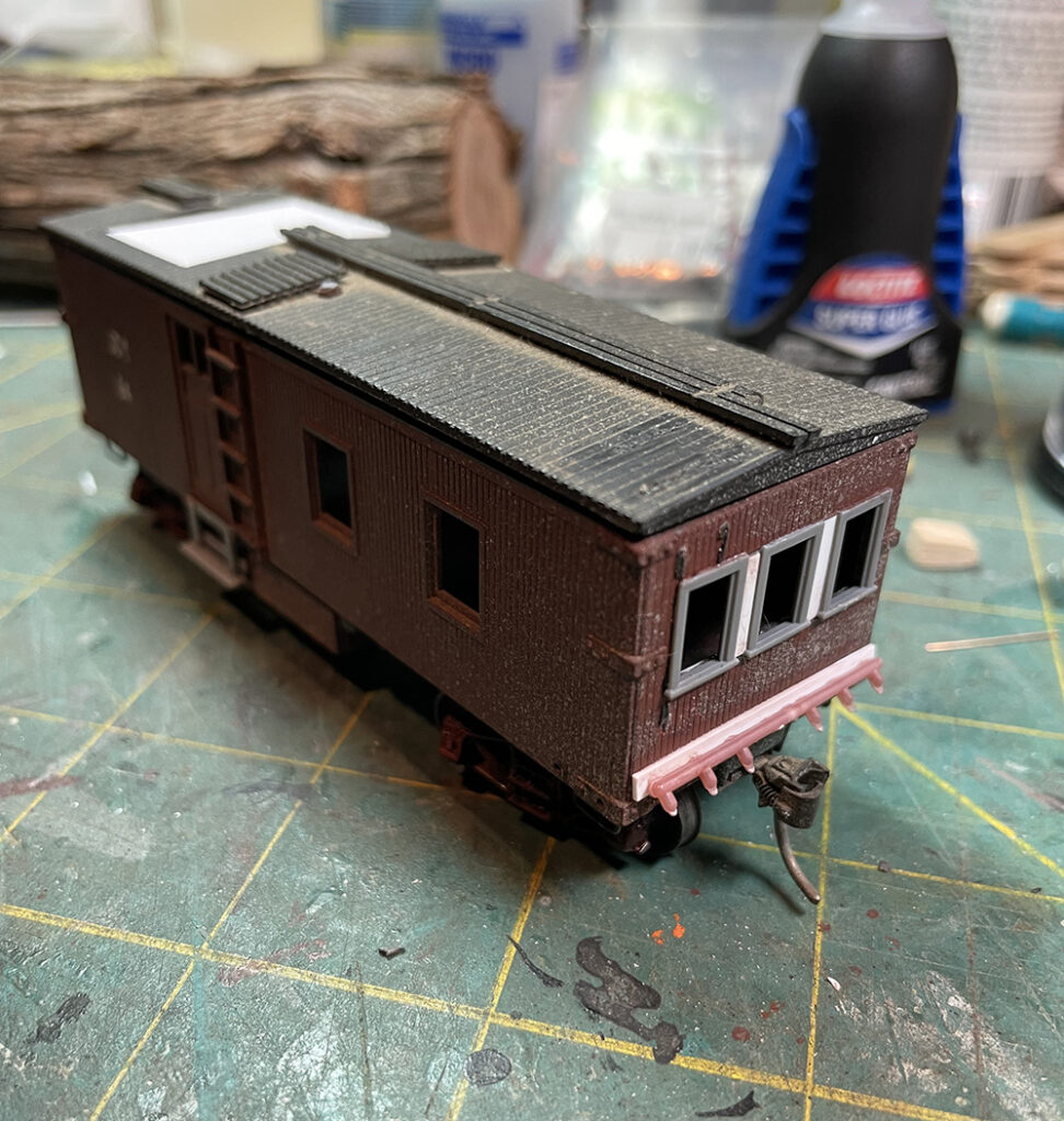 Brown model wood-sided caboose with end windows and piping along bottom front