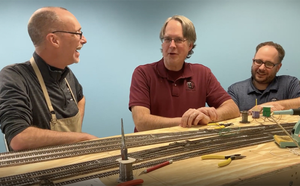 An image of three men standing at a table