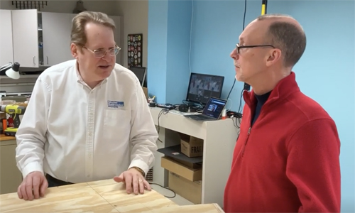 Two men speaking over a model railroad layout.
