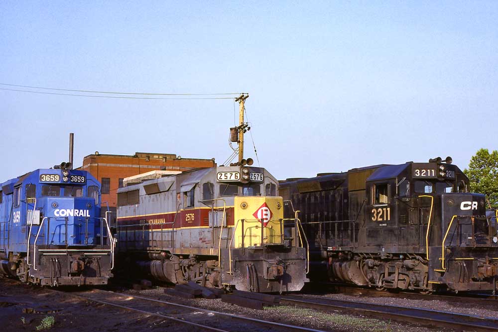Three diesel locomotives lined up in front of brick enginehouse
