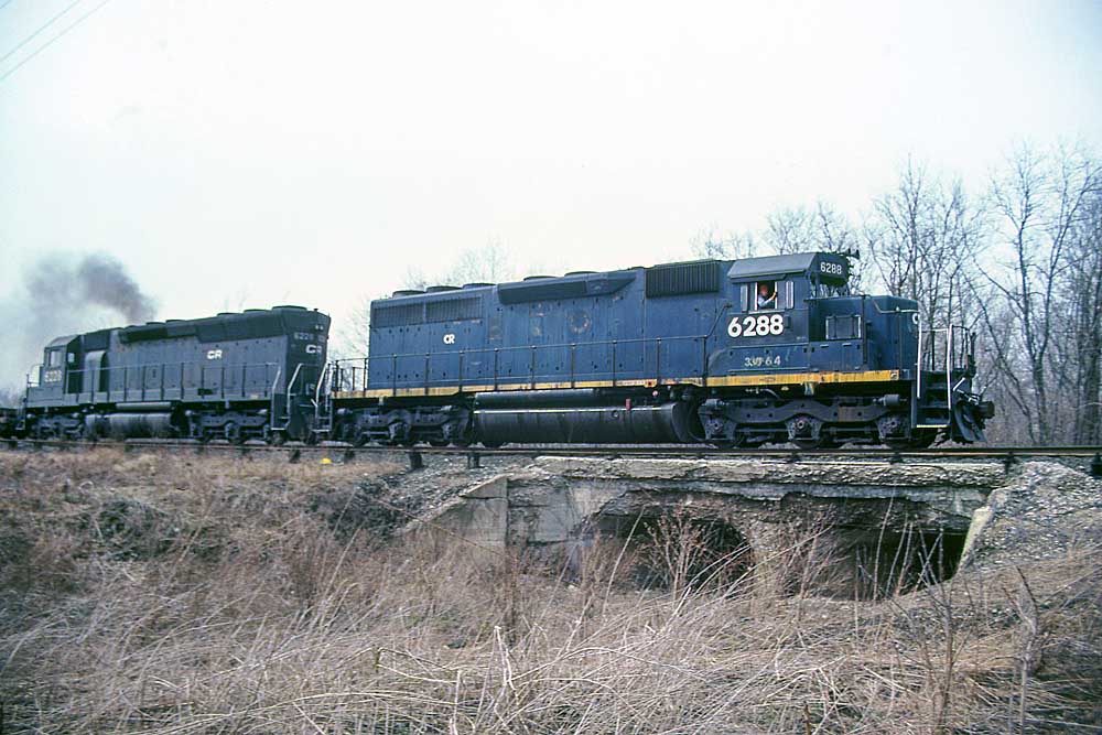 Blue-and-yellow and black diesel locomotive with freight train on low bridge
