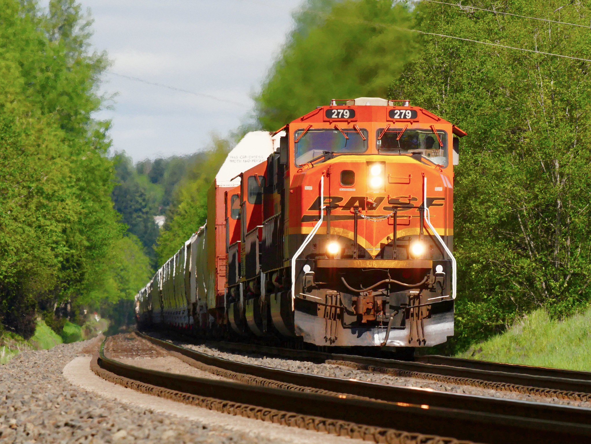 An orange and black locomotive pulling a freight train in a verdant scene.