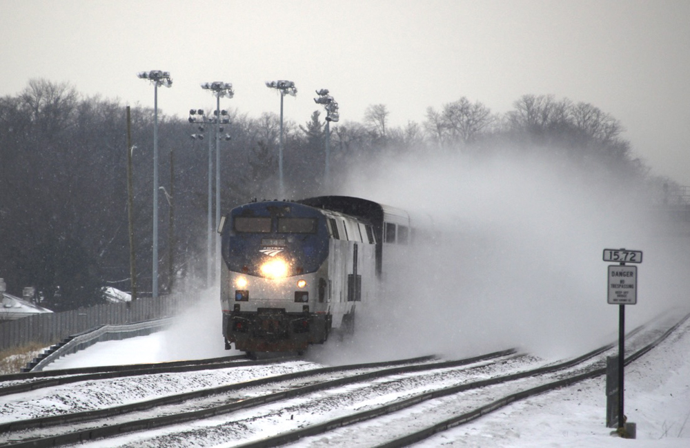 Passenger train leaves rooster tail of snow as it runs on three-track main line