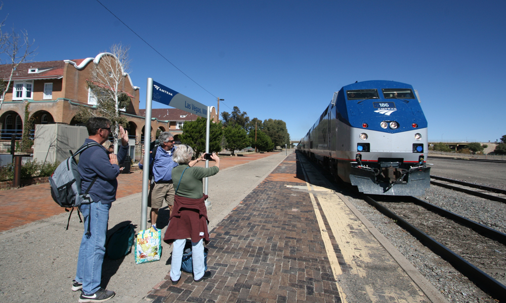 Passenger train arrives as people on platform take pictures with phoone