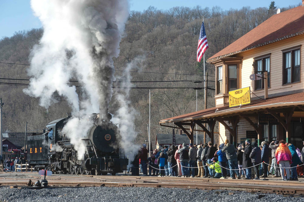 Large crowds line up in front of train station as steam locomotive prepares to move