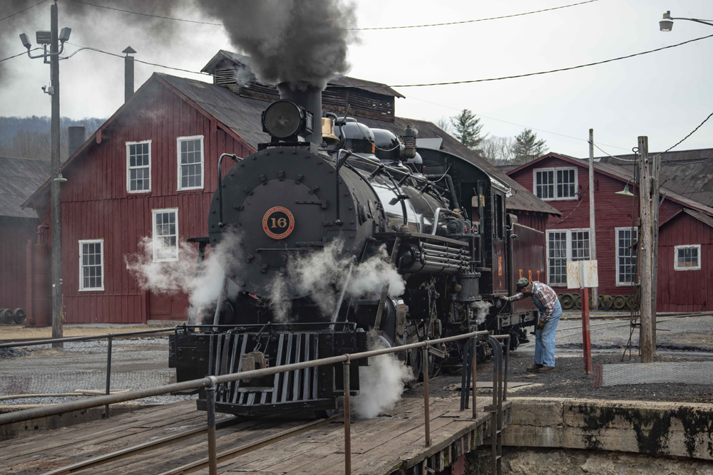 Steam locomotive at edge of turntable with red shop buildings in background