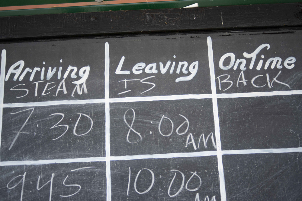 Station departure board with message "steam is back" chalked at top