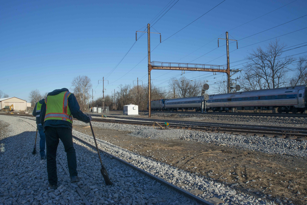 Men sweeping track as Amtrak train passes