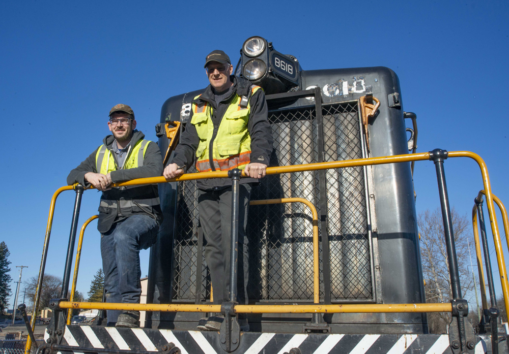 Two men standing on front of switch engine