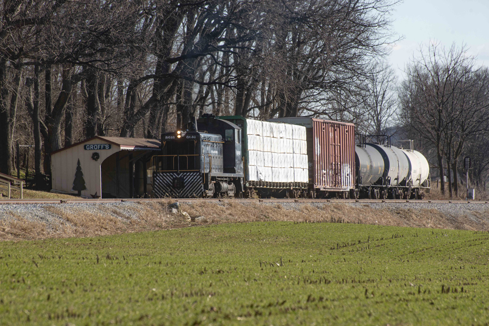 End-cab switcher with small cut of cars passes station shelter