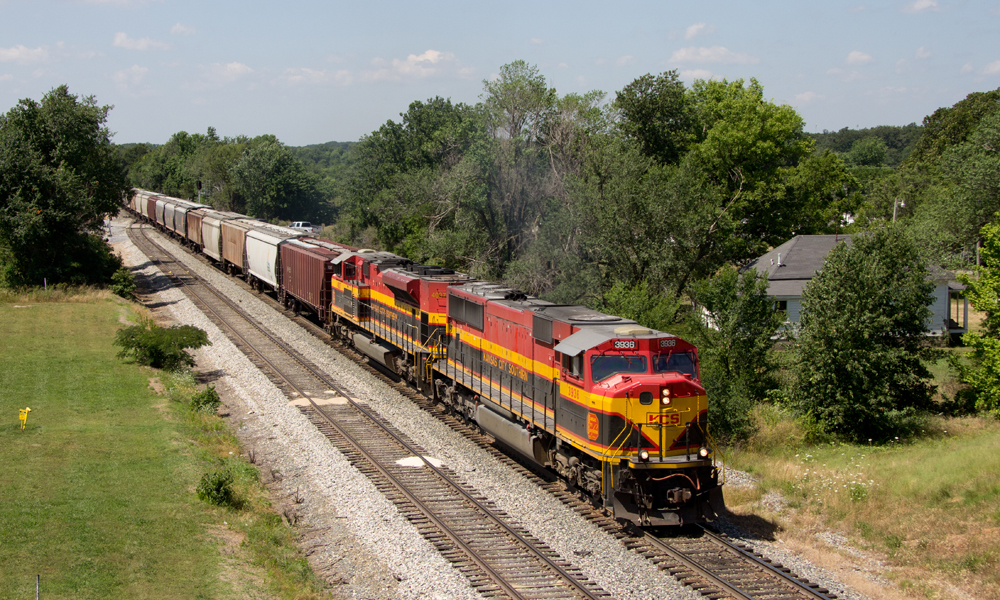 Red-yellow-and-black locomotives lead a freight train in a verdant landscape.