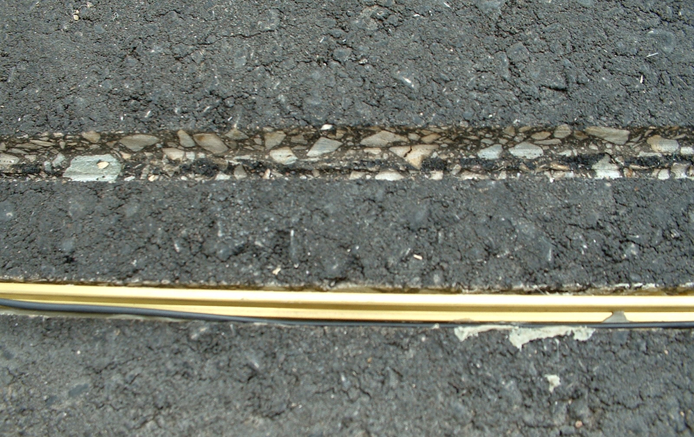 Grade crossing for a garden railway: piece of rail next to a groove cut in blacktop