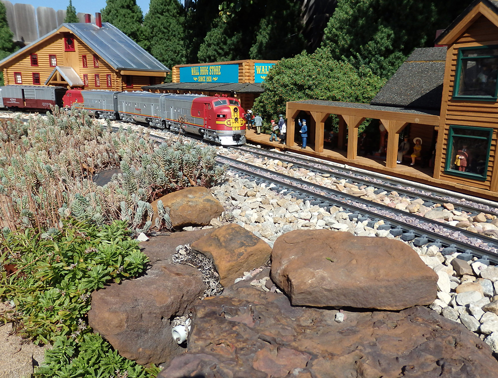 two red and silver model diesels near buildings on a garden railroad