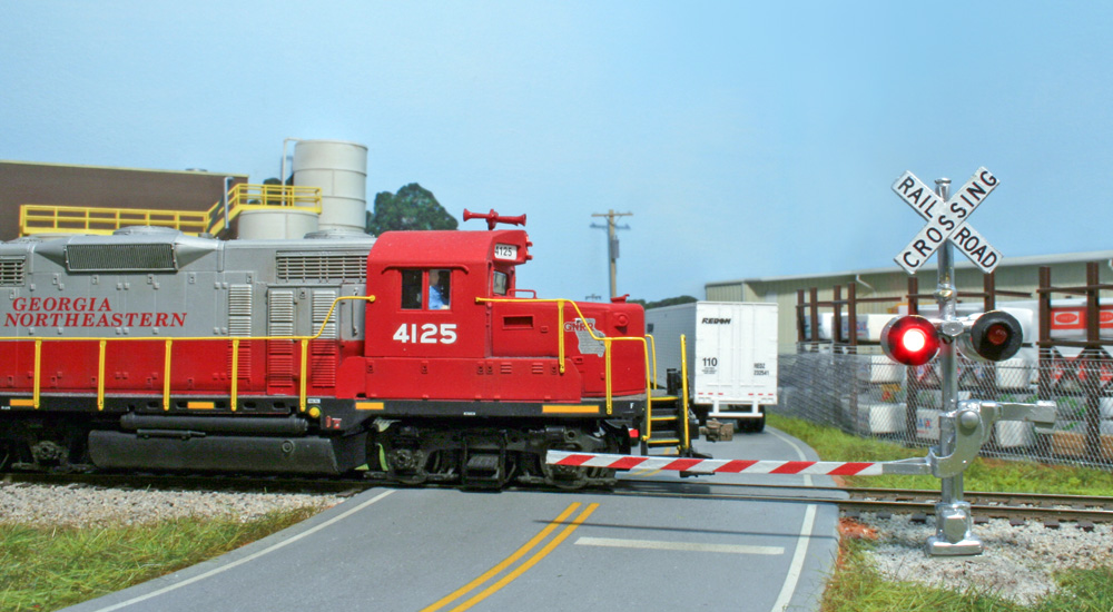 Lights on a crossing gate flash as a red-and-gray diesel crosses a road