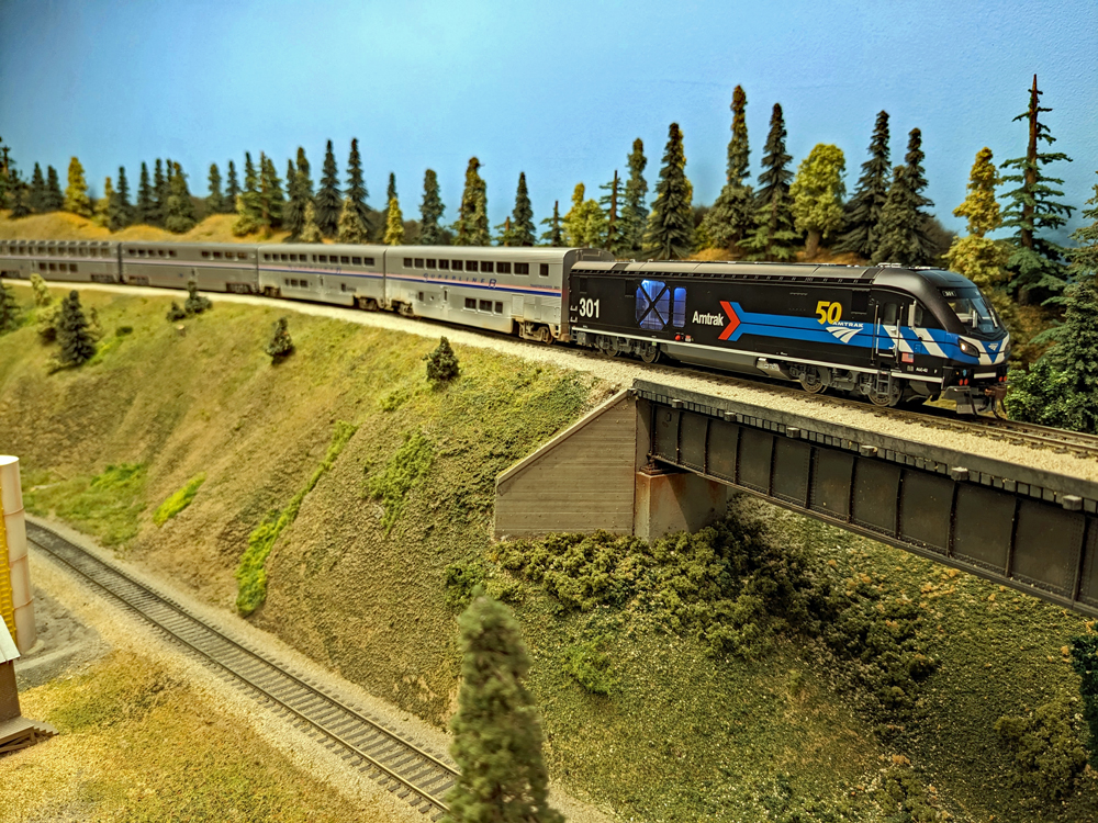 A black model diesel locomotive pulls a modern passenger train down a grade