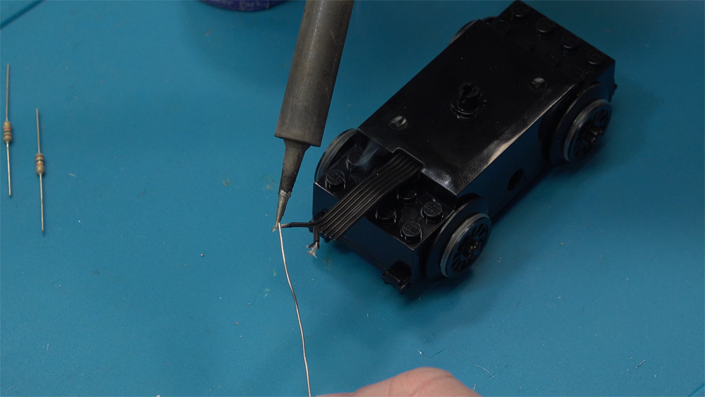 Two stripped wires protrude from a Lego train motor and are soldered