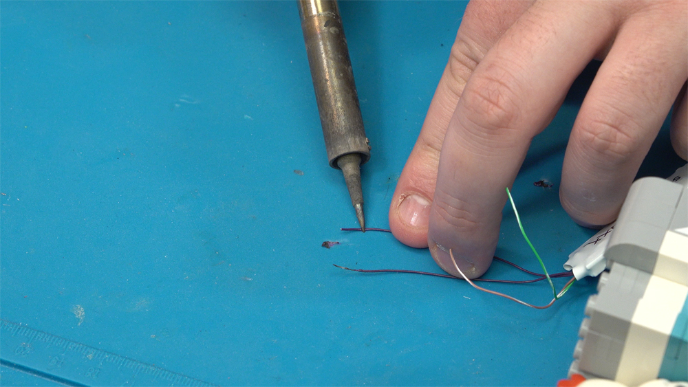 A soldering iron is held to a thin purple wire
