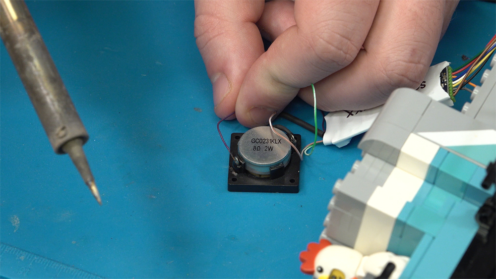 A purple wire is soldered to a contact on the backside of a speaker