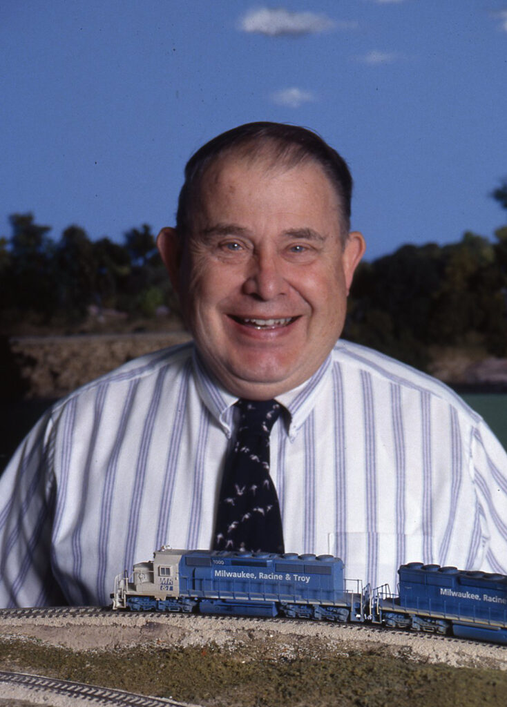 Photo of man wearing necktie with model trains in foreground.