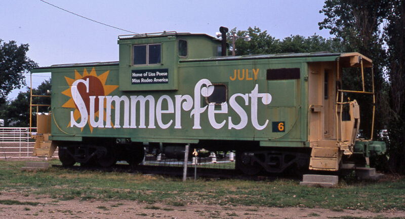 Color photo of green-and-yellow caboose with white lettering.