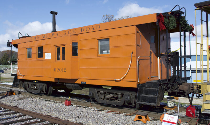 Color photo of orange caboose on sunny day.