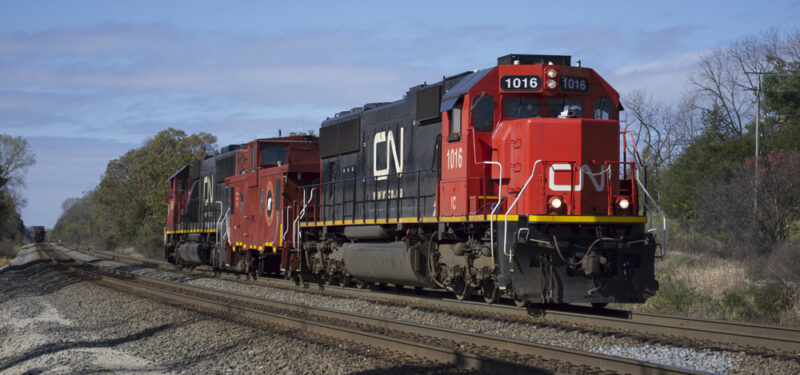Color photo of Oxide Red caboose between two locomotives painted red, white, and black.