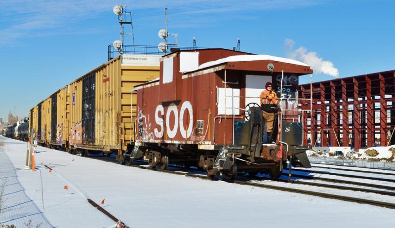 Color photo of brown-and-white caboose on a sunny, snow-covered day.