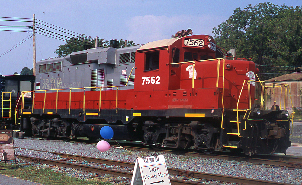 Color photo of red and silver diesel locomotive with balloons in foreground