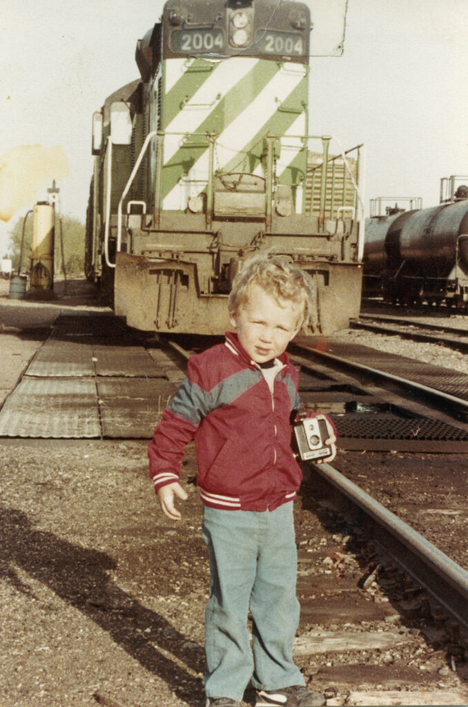 Photo of child with camera in front of a locomotive.