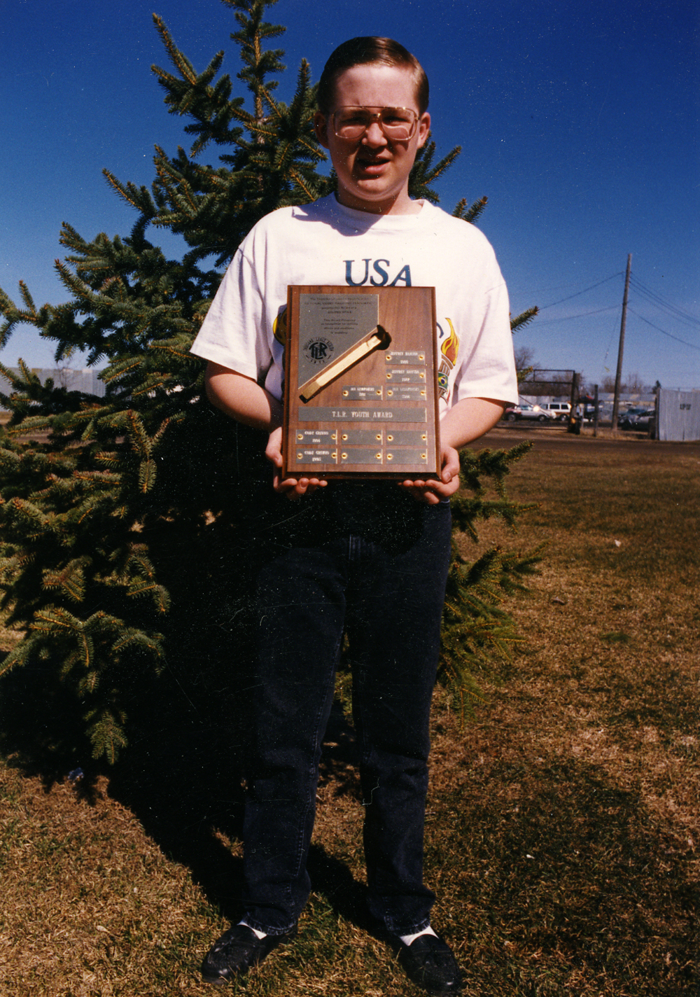 Photo of teenager standing in front of a tree with an award