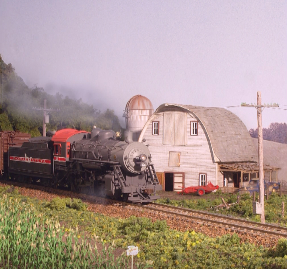 An image of a model locomotive moving past a barn