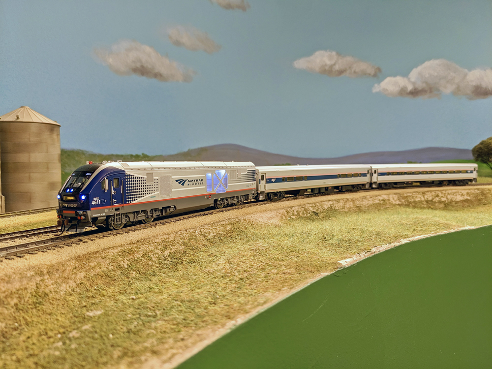 A model of an Amtrak diesel locomotive pulls two Horizon cars around a curve.