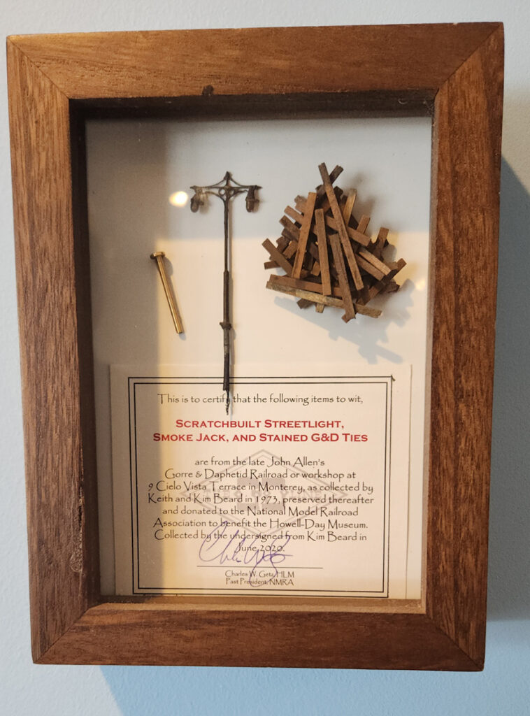 Brown picture frame holding brown sticks, a small model lamp post, and a description card