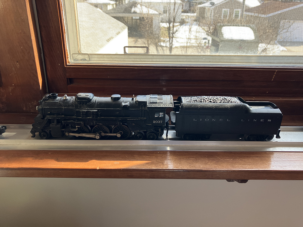 Black toy steam locomotive on silver display base resting upon brown wood windowsill