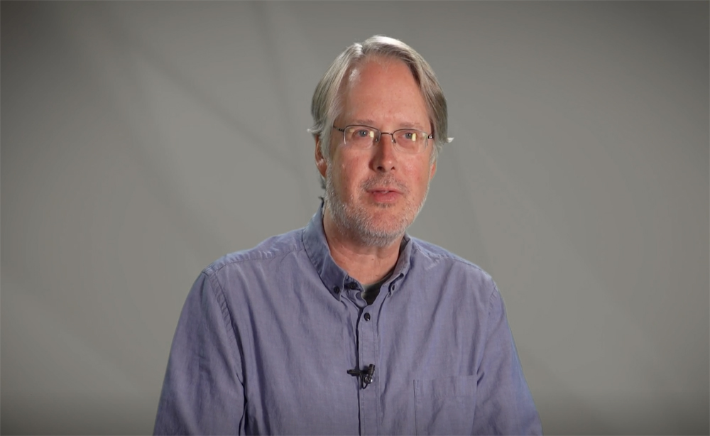Man wearing glasses and blue, collared button down shirt.