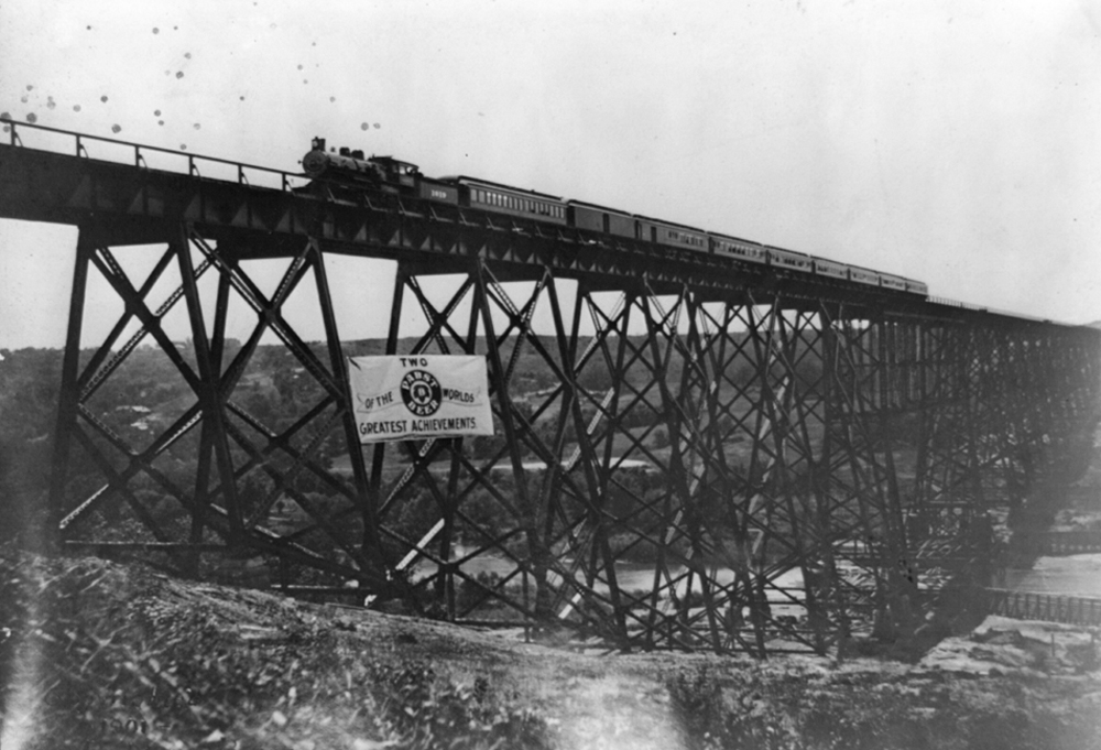 seam locomotive and passenger train on high bridge with Pabst banner on supports
