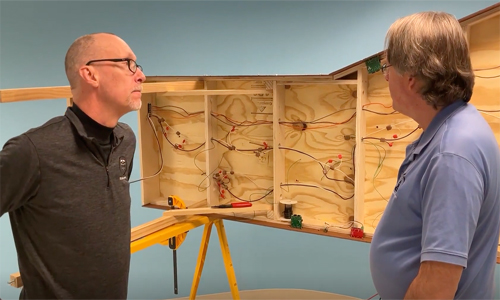 Midday Modeler for March 2, 2023: An image of two men standing in front of the underside of a model railroad layout