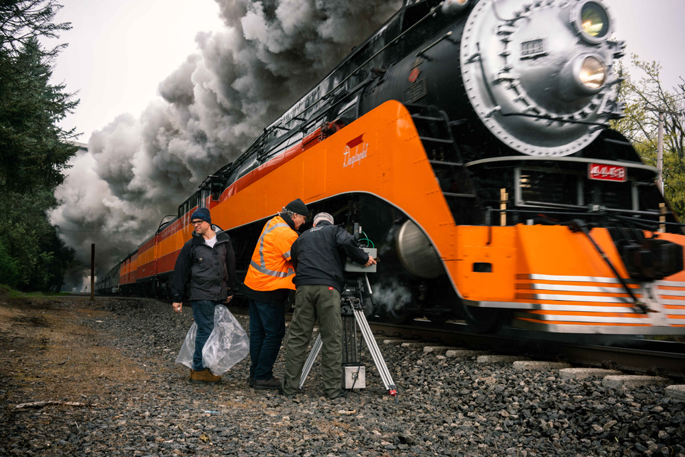 three men by orange and black locomotive