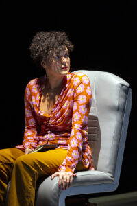 A woman in a coach seat on a stage.