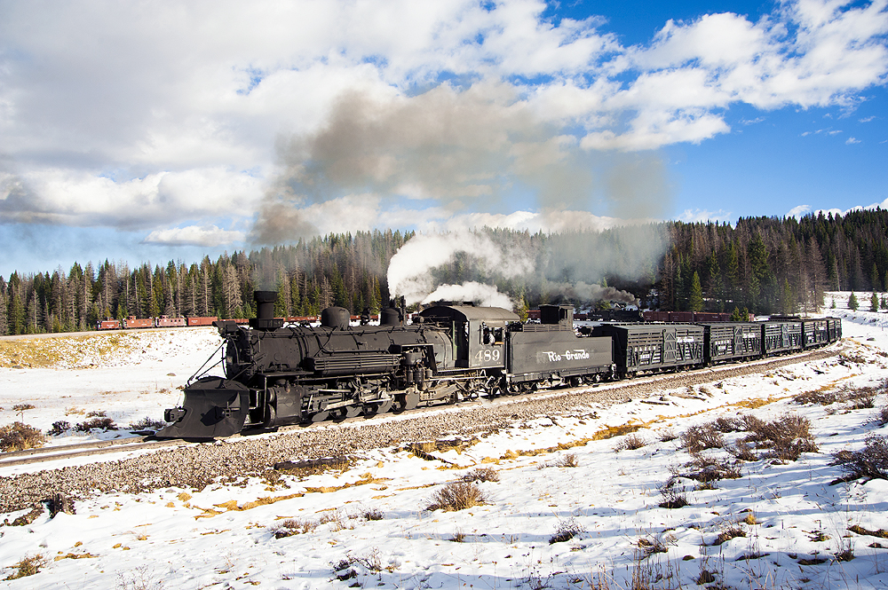 Steam locomotive leads a train through a snow landscape.