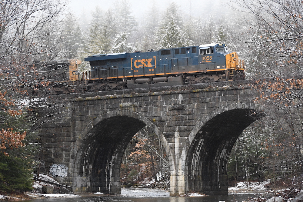 Winter photo of a blue freight locomotive on stone arch bridge