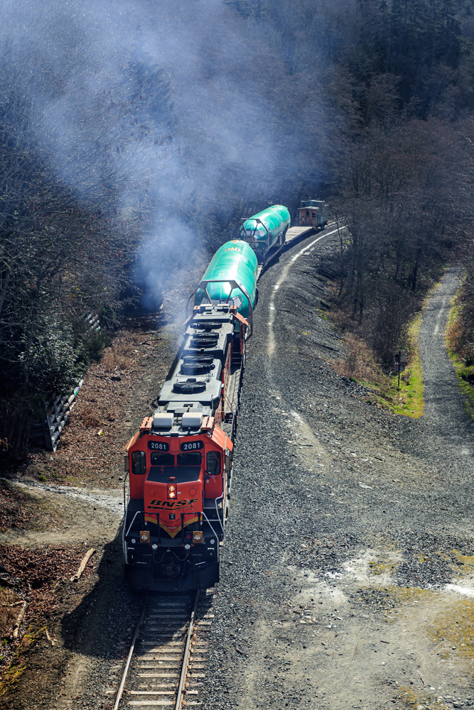 Two locomotives push flatcars with aircraft bodies up grade