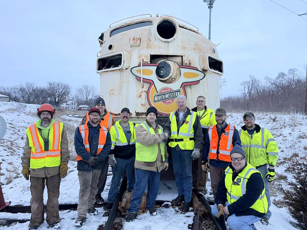 Men pose in front of weathered F7 locomotive
