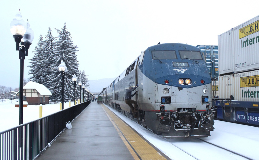 Engineer climbing into cab of diesel while passenger train is stopped at station in snow